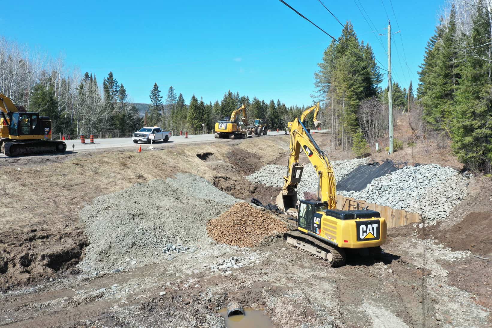 An CAT excavator is digging sand and gravel at the side of a highway during a new highway construction project by LH North.