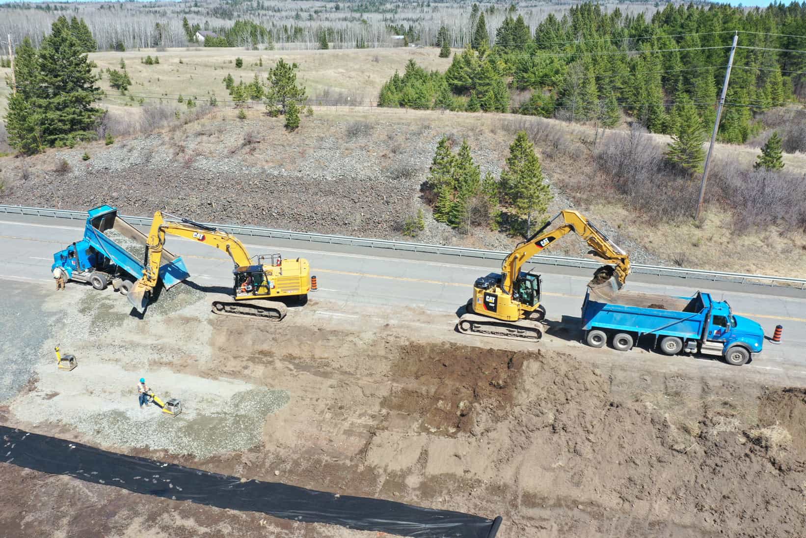 A drone view of heavy machinery busy working on a highway reconstruction site. LH North workers in full safety gear are compacting sand in the forefront.