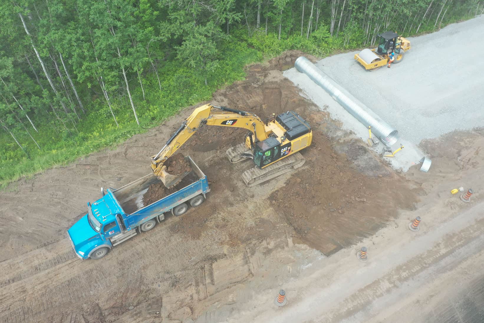 An aerial view of an CAT excavator filling a dump truck with sand on an LH North construction site. A new water pipe sits ready for installation on the right.