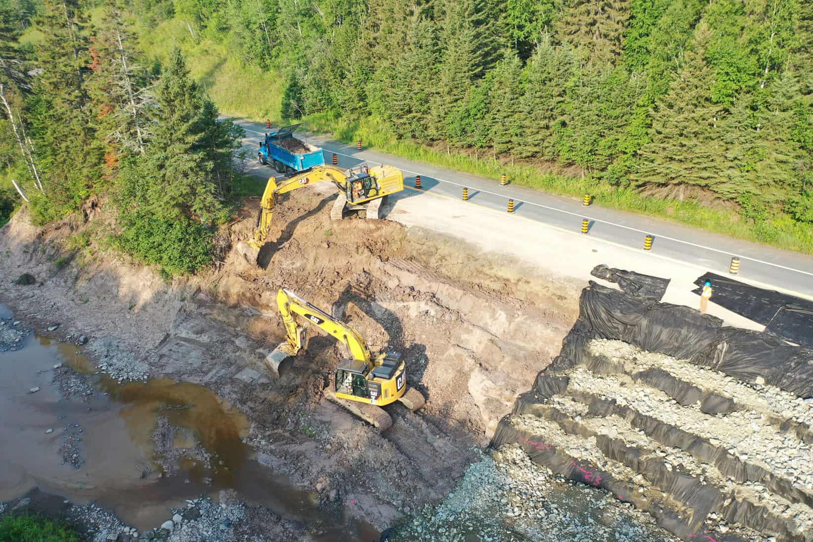 Two yellow excavators, a blue dump truck, and a plastic ramp molded in steps. This is all part of an LH North highway construction project.