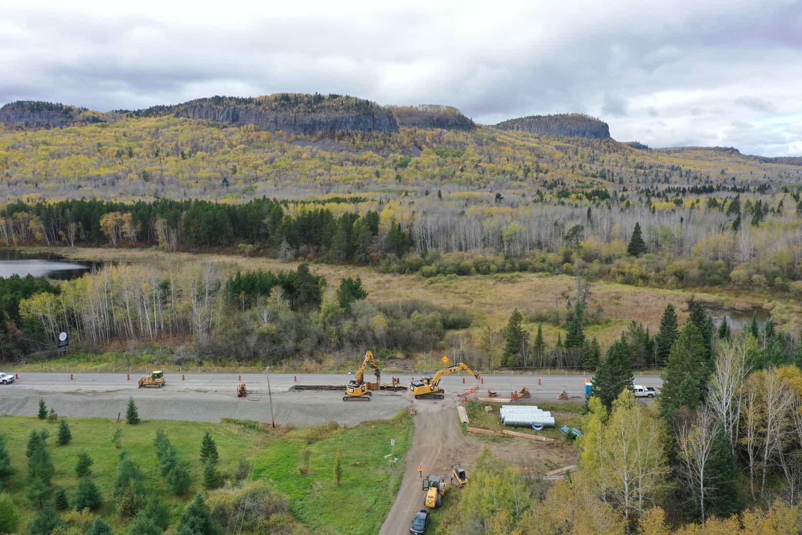 A bird's-eye view of machinery on a motorway. LH North won the contract to update this to a highway. There is pristine forest land in the background.